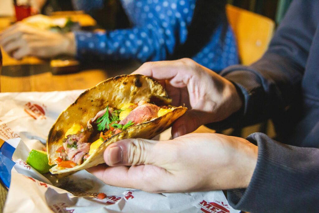 Closeup of a delicious beef taco with fresh ingredients being held at a cozy dinner setting.